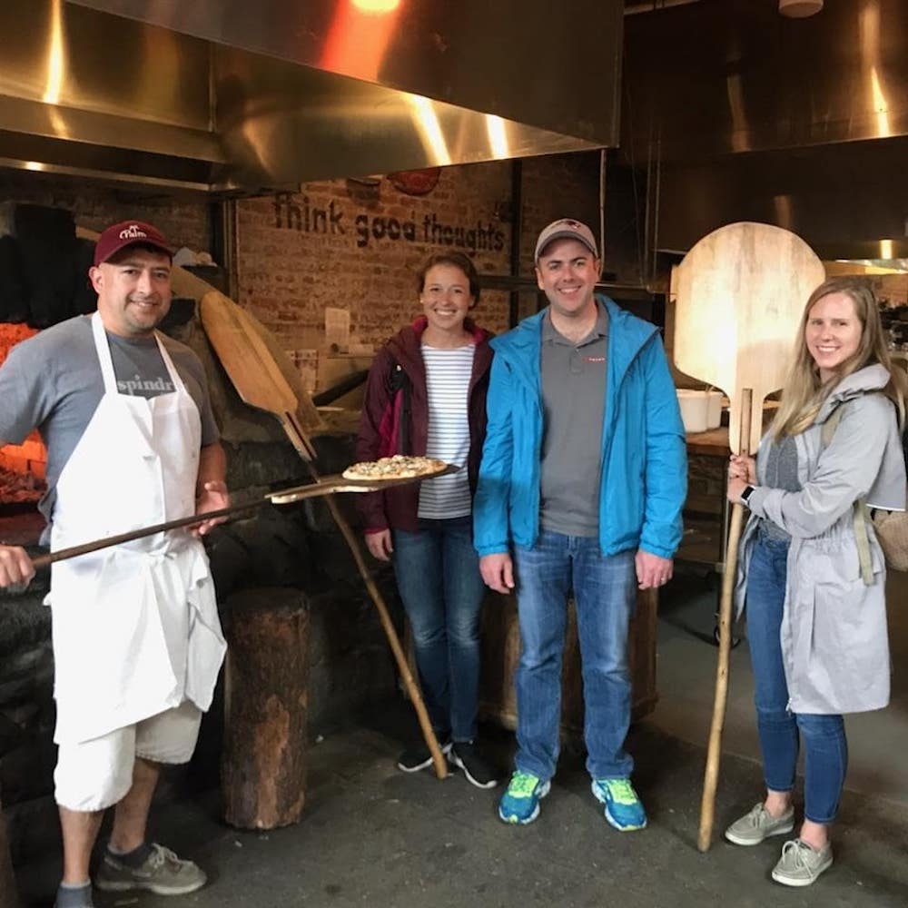 A large group of people gather in front of a pizza oven at Flatbread Pizza as seen on Off the Beaten Path Food Tours' Davis Square Food Tour.