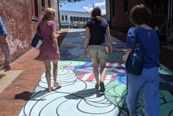 Three women walk over an art mural painted on the street while enjoying an Off the Beaten Path Food Tour in Northampton. 